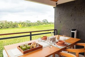 A dining table set with plates, bowls, and a tray of food, overlooking a lush green field. - Paz Tropical Villa Ubud by Omkara Experience (Bali)