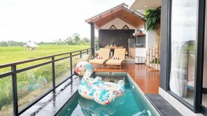 A modern outdoor pool area with a swan float, wooden deck, and a view of a green field. - Paz Tropical Villa Ubud by Omkara Experience (Bali)