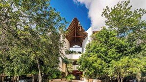 Un bâtiment doté d’une structure de toit triangulaire unique, entouré d’une végétation luxuriante et de voitures garées.