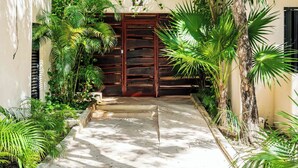 Un chemin menant à un bâtiment doté d’une porte en bois, entouré d’une végétation luxuriante et de palmiers.