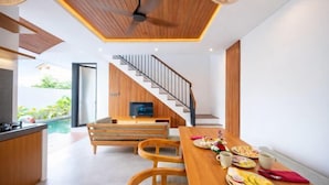 A modern kitchen with wooden cabinetry, a dining area with a wooden table and chairs, and a staircase leading to an upper level. - Omkara Dharman Ubud Villa (Bali)