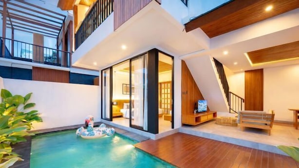 A modern indoor pool area with a floating platform, wooden flooring, and a staircase leading to an upper level. - Omkara Dharman Ubud Villa (Bali)