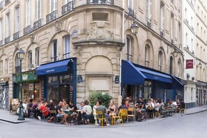An outdoor café with tables and chairs, surrounded by historic buildings with ornate facades and balconies. - A TRUE TASTE OF EVERYDAY PARISIAN LIFE, JUST MOMENTS AWAY FROM LOUVRE (Paris)