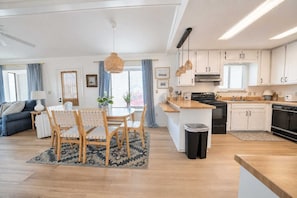 Una cocina moderna con armarios blancos, una isla central y un comedor con mesa y sillas.