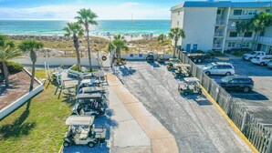 Un estacionamiento con carritos de golf, vista a la playa y un edificio con balcones.