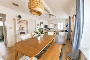 Un comedor con una mesa de madera, sillas, una lámpara colgante y vista al salón.