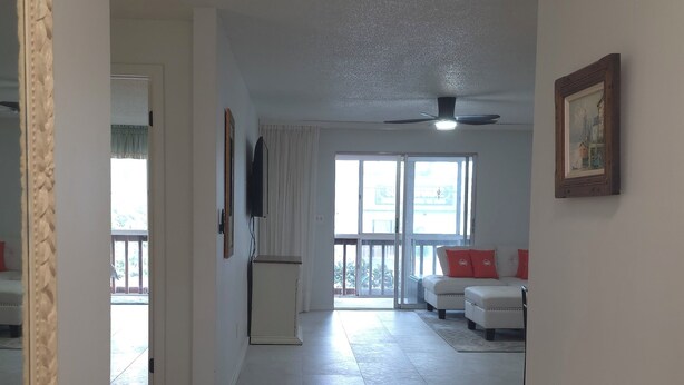 A spacious living area with a large window, a ceiling fan, and a seating area with red cushions. - Perfect Punta Gorda Location Resort Pool & Harbor (Port Charlotte)