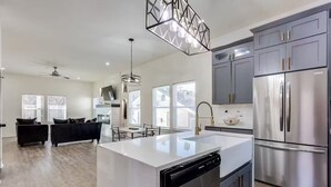 A modern kitchen with a central island, stainless steel appliances, and a dining area with a black sofa and table. - 4 bed New Construction Home near airport/downtown (Atlanta)