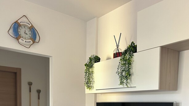 Una sala de estar moderna con televisor de pantalla plana, mueble de madera para entretenimiento y elementos decorativos como un reloj y plantas.