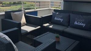 Un balcón con mobiliario de mimbre, incluyendo un sofá y sillas, y dos cojines con la inscripción 'Sweet Holiday'.