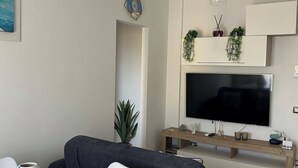 Una sala de estar moderna con un sofá gris, una mesa redonda blanca y un televisor instalado en un mueble de madera.