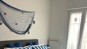 Un dormitorio con una cama, ropa de cama a rayas azules y blancas, un cabecero gris y almohadas azules.