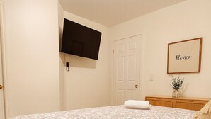A bedroom with a floral-patterned bedspread, a flat-screen TV mounted on the wall, a door, and a framed 'blessed' sign. - Peaceful 2-bedroom townhome with AC in Lawrenceville (Lawrenceville)