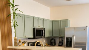 A modern kitchen with green cabinets, a stainless steel refrigerator, a coffee maker, and two gold stools. - Peaceful 2-bedroom townhome with AC in Lawrenceville (Lawrenceville)