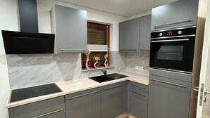 Een moderne keuken met grijze kastjes, een zwart fornuis en een marmeren spatwand.