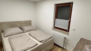 Een kleine, moderne slaapkamer met een eenpersoonsbed, een raam met zonwering, een radiator en een houten vloer.