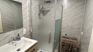 Een moderne badkamer met een douchecabine van glas, een wit wastafelmeubel met een zeepdispenser en een houten vloer.