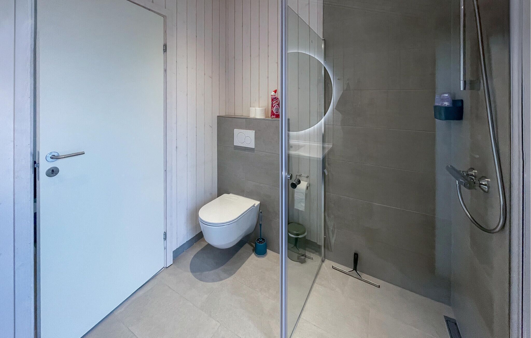 A modern bathroom with a toilet, a glass shower enclosure, and a white door.