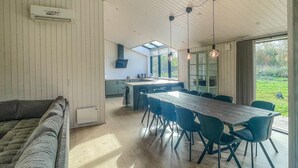 A modern kitchen with a central island, a dining area with a long table and chairs, and a cozy seating area with a sofa.