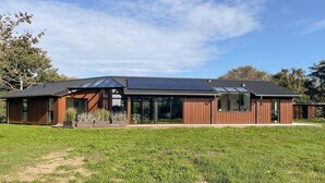 A modern house with a large glass facade, solar panels, and a well-maintained lawn.