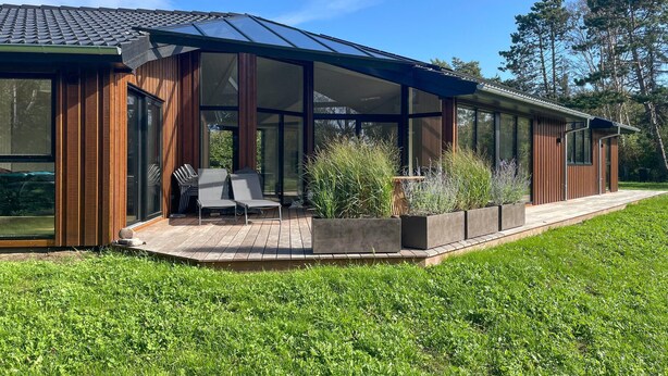 A modern house with a glass conservatory, wooden exterior, and a patio with outdoor seating.
