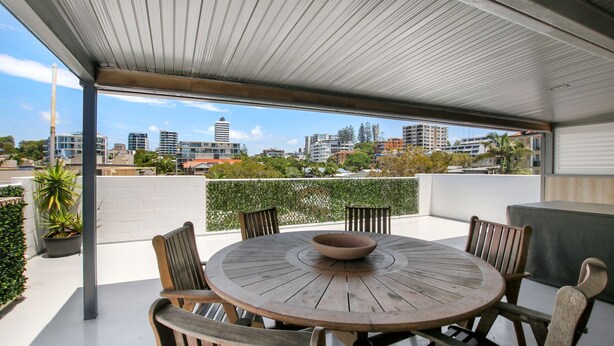 A round wooden table with chairs and a bowl, set on a balcony with a view of city buildings. - Trade Winds Unit 5, 52 Edmund St, Kings Beach (Kings Beach)