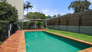 A rectangular swimming pool with a tiled deck, surrounded by a wooden fence and a grassy area. - Trade Winds Unit 5, 52 Edmund St, Kings Beach (Kings Beach)