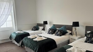 A hotel room with two single beds, each with a green bedspread and white pillows. There are two bedside tables with lamps, and a window with sheer curtains. - Room 9 -  Manor Park Country House, Wales Perfect for Families (Swansea)