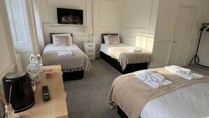 Quarto de hotel com duas camas, uma escrivaninha com cafeteira e uma televisão na parede.