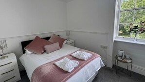 Een keurig opgemaakt hotelkamer met een bed, nachtkastjes, een tafeltje met een bloevas en een raam met uitzicht op groen.