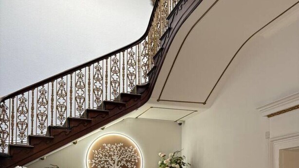 Una imponente escalera con barandillas ornamentales, un elemento decorativo circular iluminado y arreglos florales.