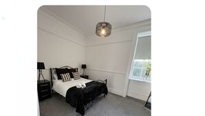 Un dormitorio con cama, mesitas de noche, lámpara y ventana.