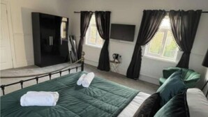 Een slaapkamer met een bed, een kledingkast, een televisie en een raam met gordijnen.