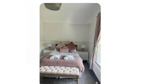 Ein ordentlich eingerichtetes Schlafzimmer mit Bett, Nachttischen, einer Bank und einem Fenster mit Vorhängen.