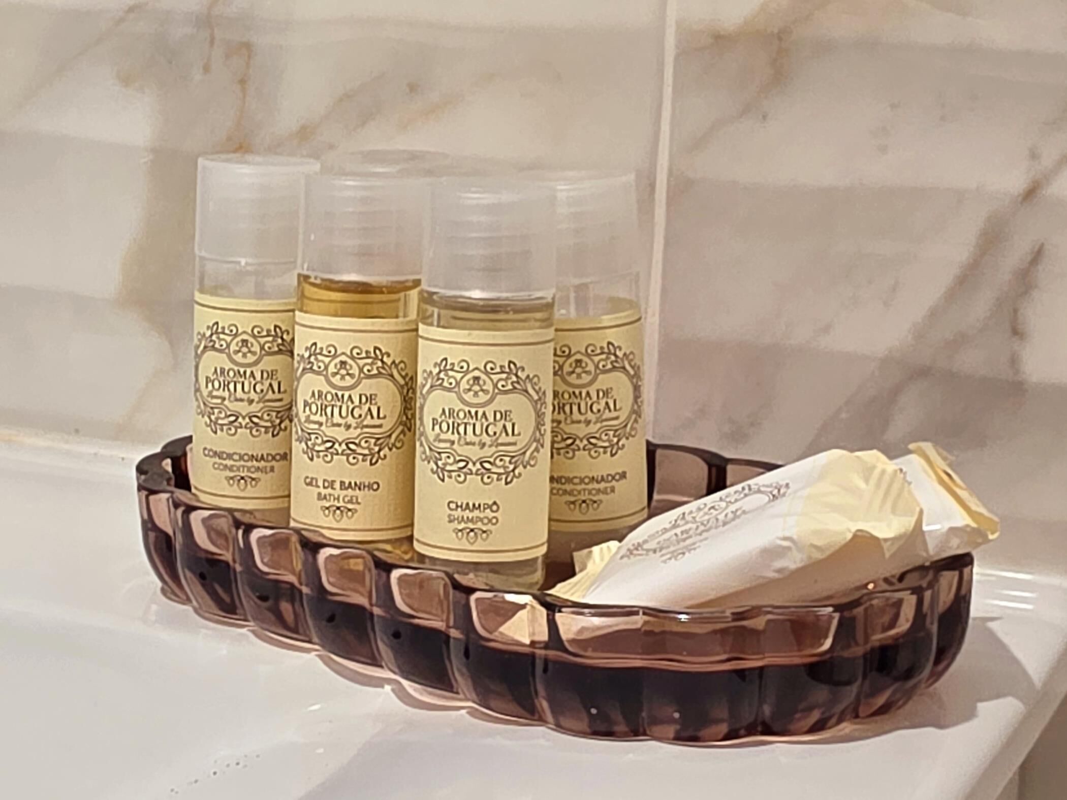 Una repisa de baño con cuatro botellas de productos 'Aroma de Portugal' y una pastilla de jabón.
