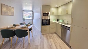 A modern kitchen with a dining area, featuring a wooden table, chairs, and a window with a view of trees. - Aconchego da Vila | Olival Flat | Castelo de Vide (Castelo de Vide)