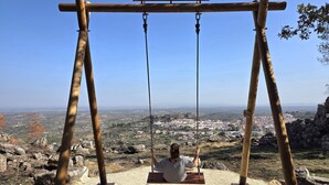 A wooden swing set with a sign reading "CASTELO DE VIDE. UM LUGAR NA MEMÓRIA" and "Freguesia de São João Baptista" against a clear sky. - Aconchego da Vila | Olival Flat | Castelo de Vide (Castelo de Vide)