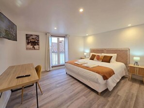 Quarto de hotel com cama, escrivaninha, cadeira, mesa de cabeceira e janela com vista.