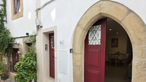 A building with a stone archway entrance, a red door, and a white door with a number plate. - Aconchego da Vila | Serra Flat | Castelo de Vide (Castelo de Vide)