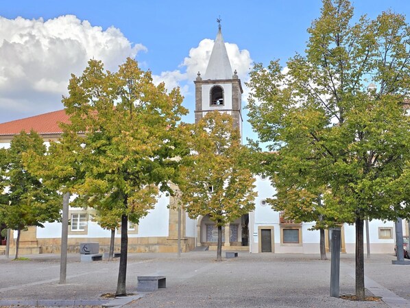 A courtyard with a church tower, trees, and a paved area.