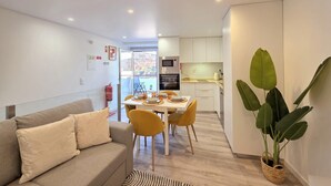 A modern living room with a sofa, a dining table with chairs, a kitchen area with appliances, and a large plant. - Aconchego da Vila | Serra Flat | Castelo de Vide (Castelo de Vide)