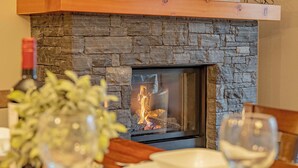 Una chimenea con revestimiento de piedra, una mesa de comedor con un plato blanco y una copa, y una botella de vino.