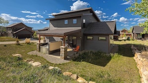 A modern two-story house with a patio, stone accents, and a view of neighboring homes. - Trailside Location | Mountain Escape (Granby)