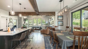 A spacious kitchen with a large island, wooden ceiling beams, and a dining area with a table set for six. - Trailside Location | Mountain Escape (Granby)