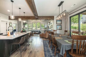 A spacious kitchen with a large island, wooden ceiling beams, and a dining area with a table set for six. - Trail Views | Hot Tub (Granby)