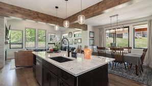 A modern kitchen with a large island, wooden beams, and large windows. - Trailside Location | Mountain Escape (Granby)