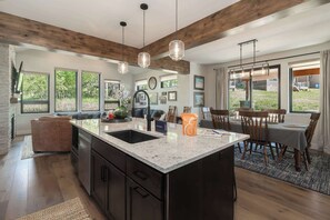 A modern kitchen with a large island, wooden beams, and large windows. - Trail Views | Hot Tub (Granby)
