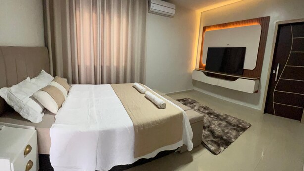 A modern bedroom with a bed, a TV mounted on the wall, and a door.