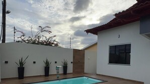 A rectangular swimming pool with a wooden deck, surrounded by a low white wall and potted plants.