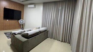 A modern living room with a sofa, a flat-screen TV, an air conditioner, and a ceiling fan.